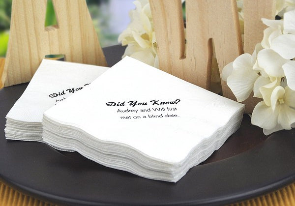 Stack of personalized wedding napkins with custom text on a black plate surrounded by white flowers