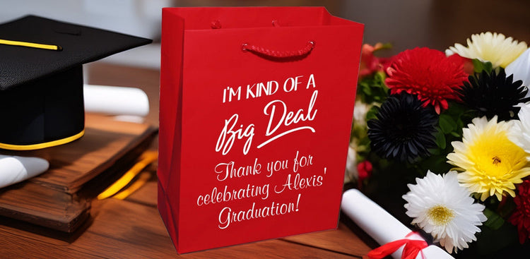 Red personalized graduation gift bags with celebratory messages next to graduation cap, diploma, and colorful flowers