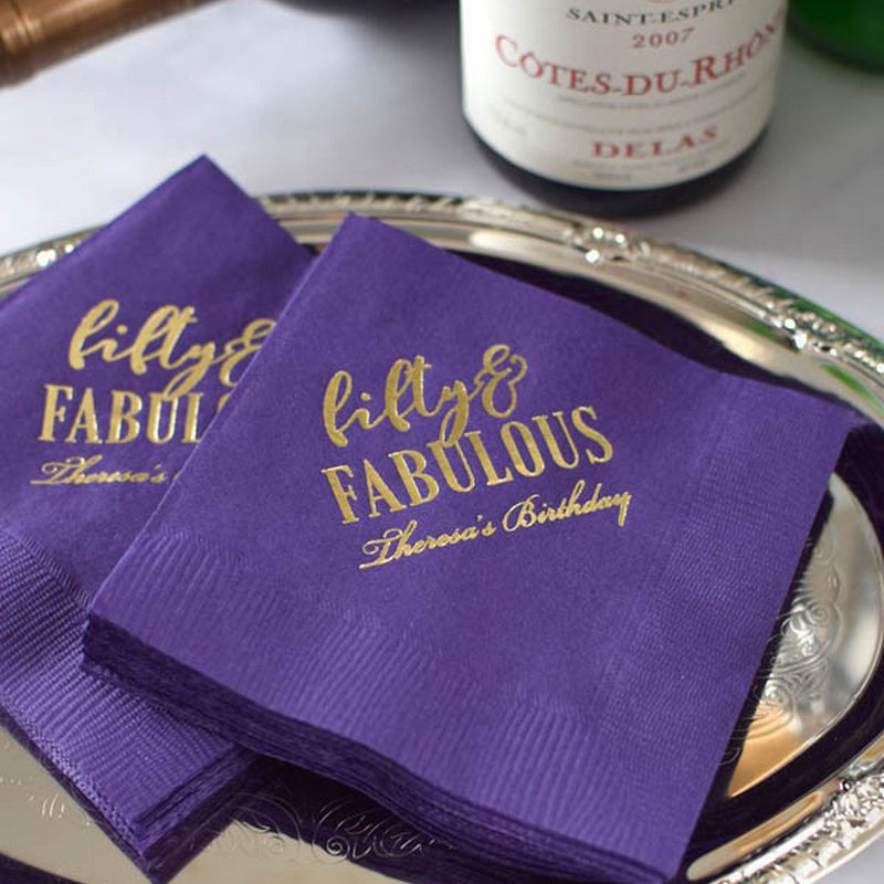 Purple personalized birthday party napkins for adults with gold foil text fifty and fabulous on silver tray