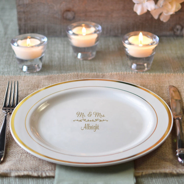 Elegant personalized plastic wedding plates with gold trim and custom names set with candles and cutlery