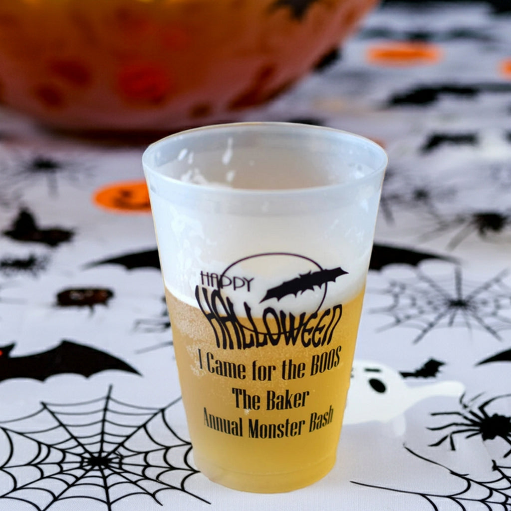Personalized Halloween cup in front of a punch bowl on a Halloween theme table cloth