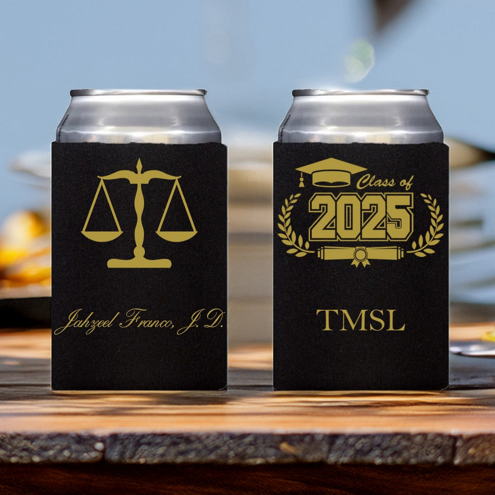 Two can cooler sleeves personalized for a graduate from law school in gold print setting on an outdoor table. The can sleeve on the left is personalized with a scales of justice graphic with the graduate's name printed below in a formal script font. The can sleeve on the right is personalized with a "Class of 2025" design featuring a graduation cap and diploma wrapped with wheat stalks and the initials "TMSL" for "Thurgood Marshall School of Law" in a bold italic font.