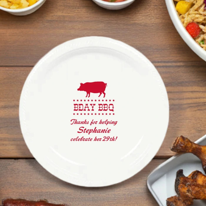 White plastic birthday party plate personalized with Bday BBQ design and custom text in red print on picnic table with appetizers