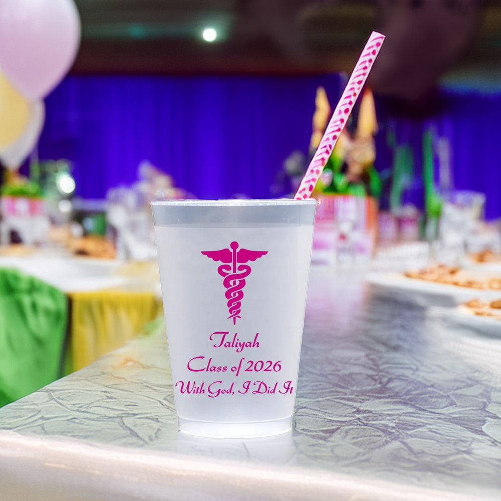 Small frosted plastic cups personalized for nursing school graduation with Caduceus design and text "Taliyah, Class of 2026, With God, I Did It!" in fuschia print