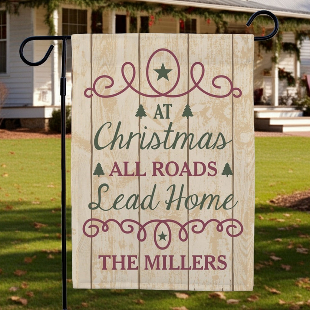 Christmas garden flag featuring a rustic design with the phrase At Christmas All Roads Lead Home The Millers