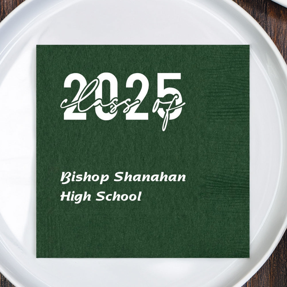 A forest green color paper luncheon napkin personalized in square layout form for a graduation party in white print. Two lines of custom text are printed below a Class of 2025 graphic design. The two lines of custom text are the name of the graduate's high school in a fun italic font. The napkin is centered on a white plastic serving plate.