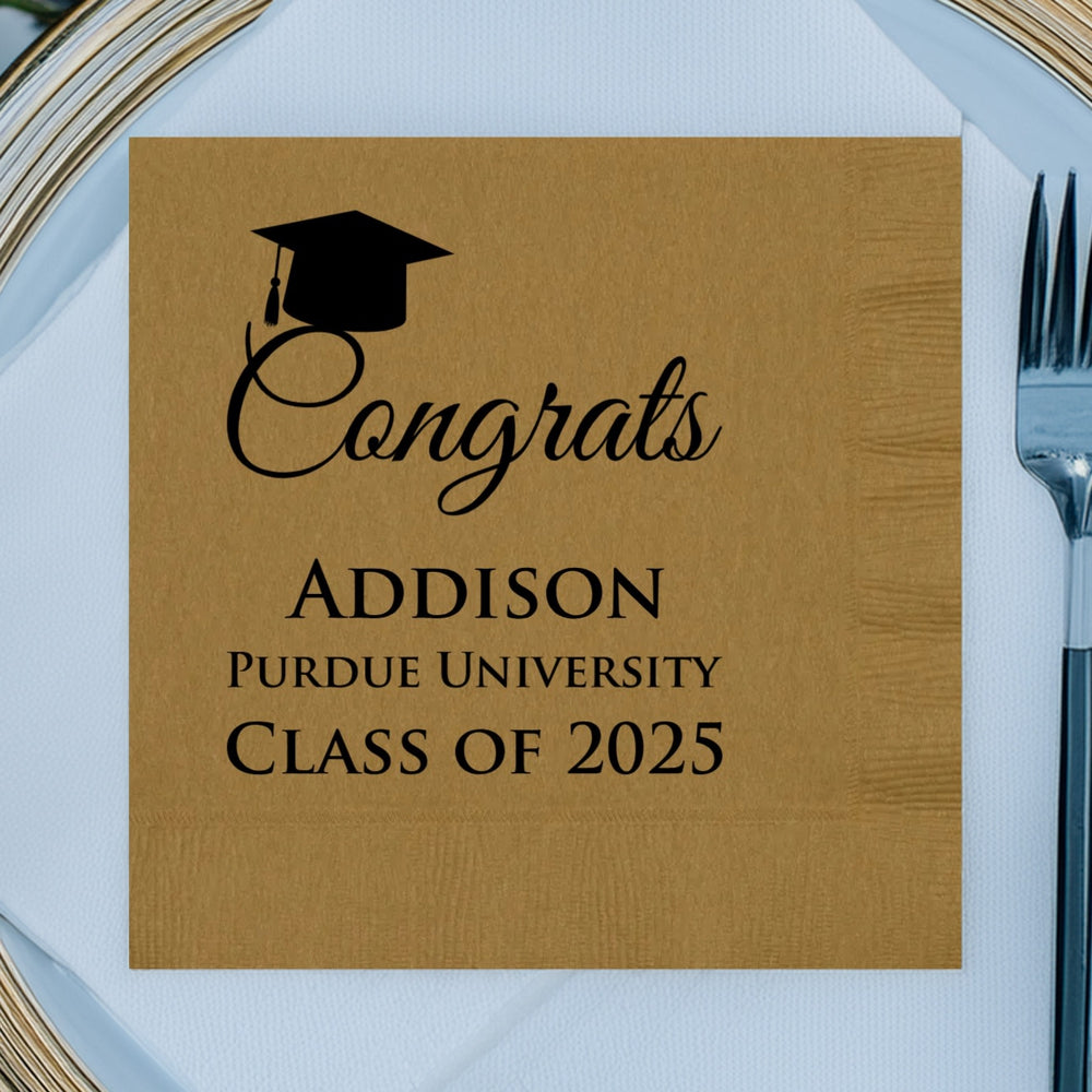 A gold, square-oriented graduation napkin personalized with black print featuring silhouette of a graduation cap with a tassel at the top.
Below the cap, the word "Congrats" is printed in cursive font with the graduate's name displayed in large, bold, block letters. "Purdue University" is printed in smaller, bold, lettering below the graduate's name. The wording "Class of 2025" is displayed in bold letters. The napkin is laying on top of a white linen napkin over a white charger with gold trim.