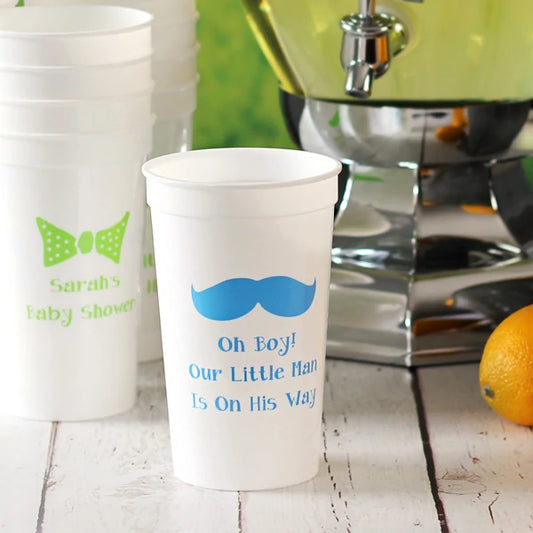 White 22 oz. stadium cups persoanlized for baby sower with bow tie design and three lines of custom text in neon green print and mustache design and 3 lines of text in blue print