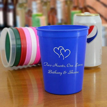 Blue 16 oz. stadium personalized with double hearts design and 2 lines of custom text in white imprint color for wedding reception drink cups
