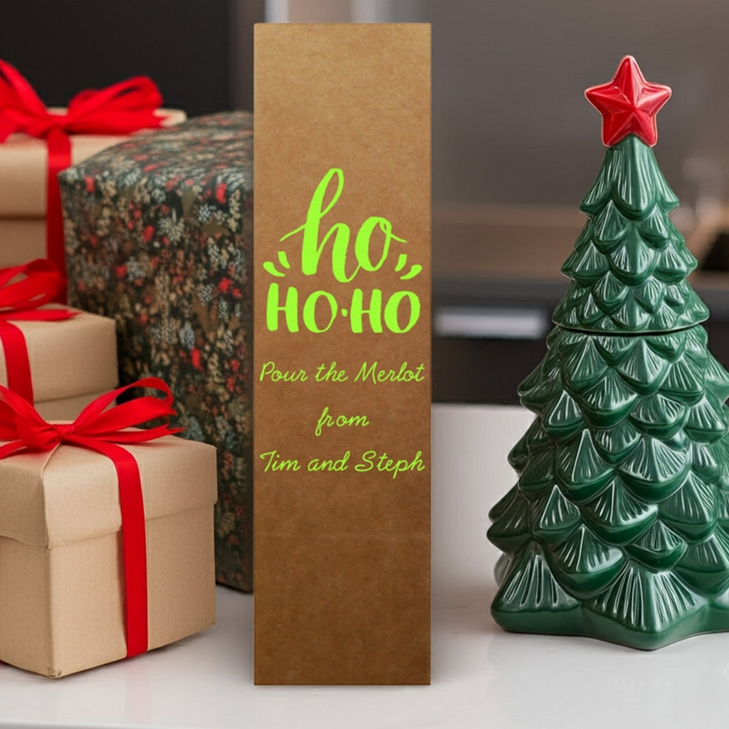 Brown wine bottle bag with green ho ho ho text near gifts and tree foil stamped personalized Christmas wine bottle gift boxes