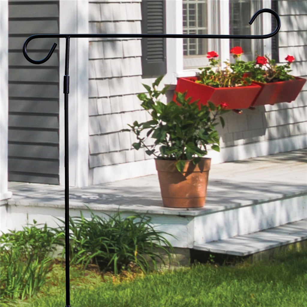 Black metal garden flag stand displayed in front of a house with a porch and potted plants