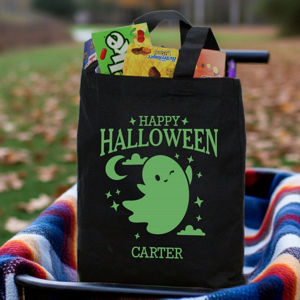 Black tote with green ghost design and name Carter on a glow in the dark ghost personalized trick or treat bag filled with candy