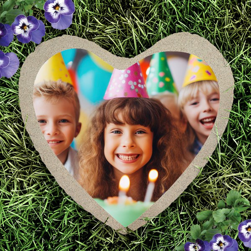 Heart shape custom photo garden stone with a kids birthday party picture displayed on grass with purple flowers