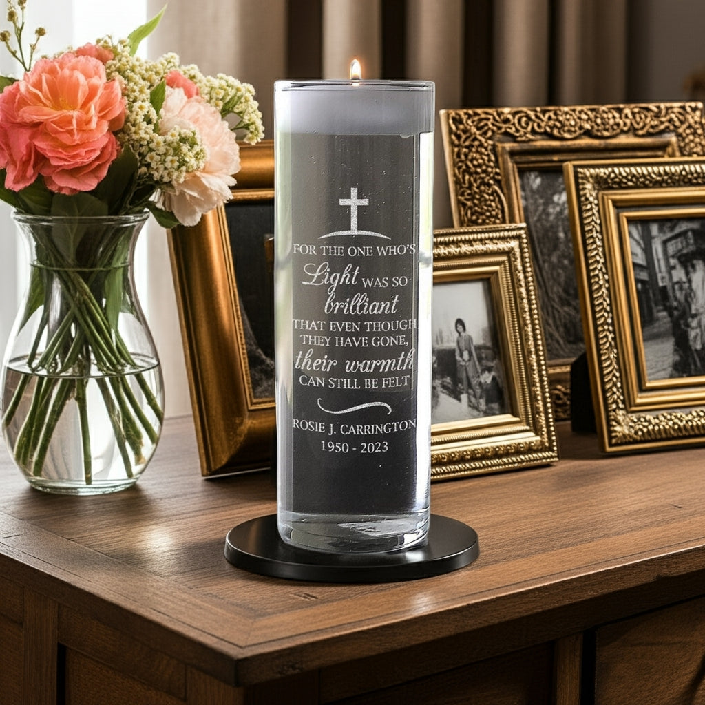 Personalized memorial candle vase with engraved tribute text displayed on wooden table with flowers and photo frames