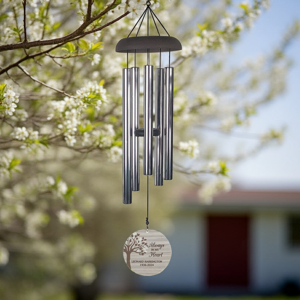 Personalized memorial wind chime with engraved wooden heart hanging outdoors in blooming tree