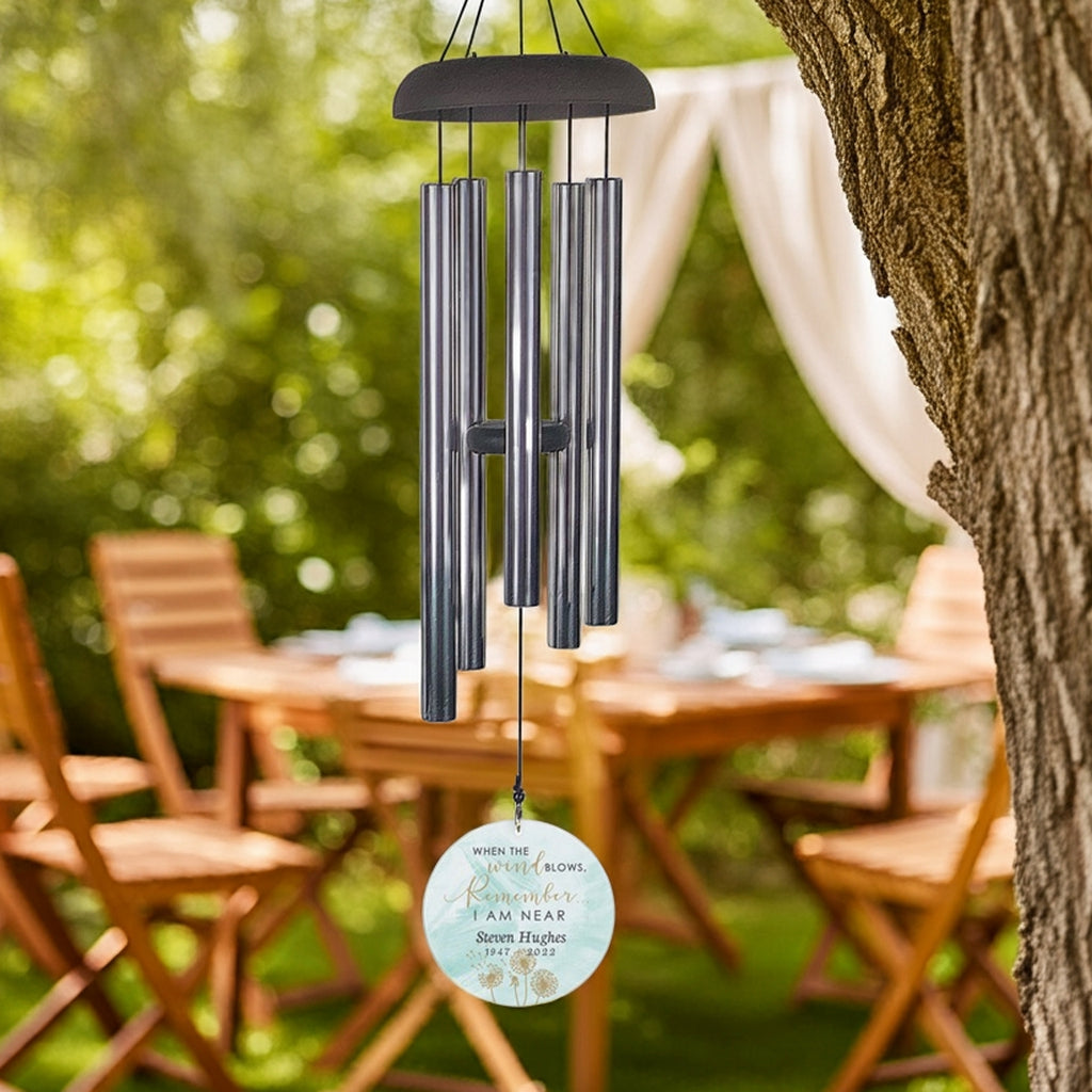 Personalized memorial wind chime hanging from tree with engraved remembrance disc in outdoor garden setting