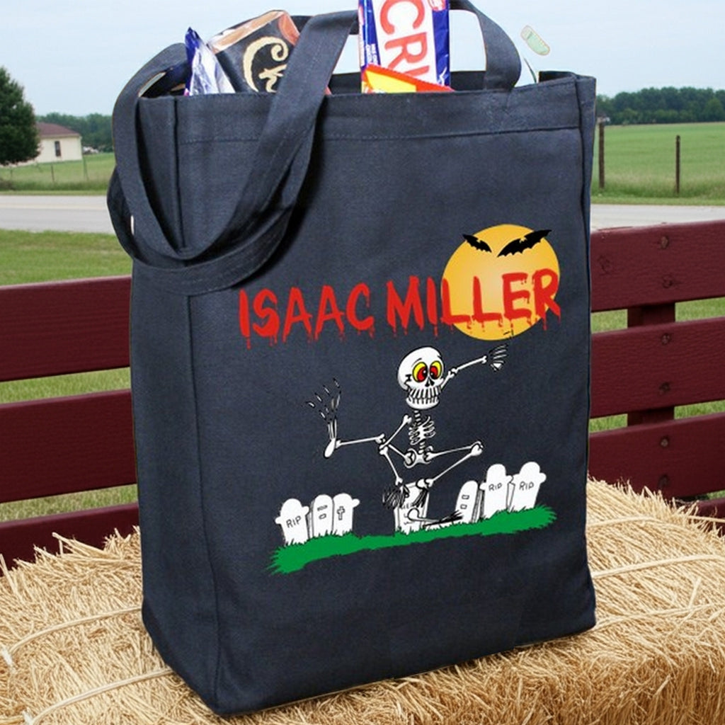 Black Halloween tote with skeleton graveyard design and red name ISAAC MILLER personalized trick or treat bag filled with candy
