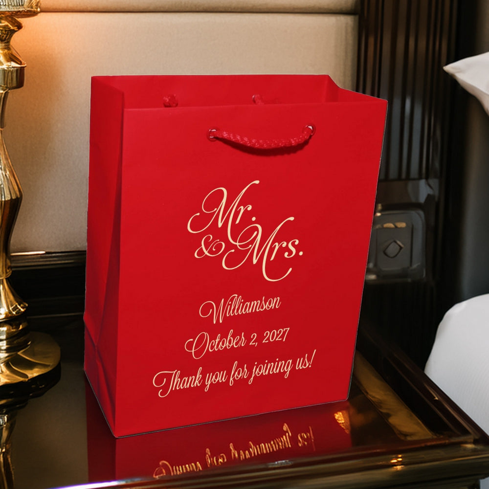 Red wedding gift bag with gold Mr and Mrs script and personalization on bedside table wedding welcome bags custom printed