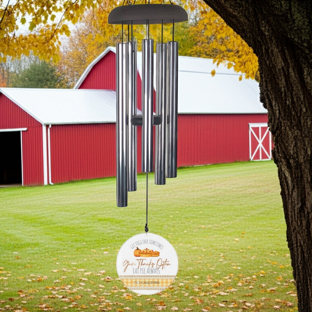 Personalized wind chime with metal tubes hanging from tree in front of red barn