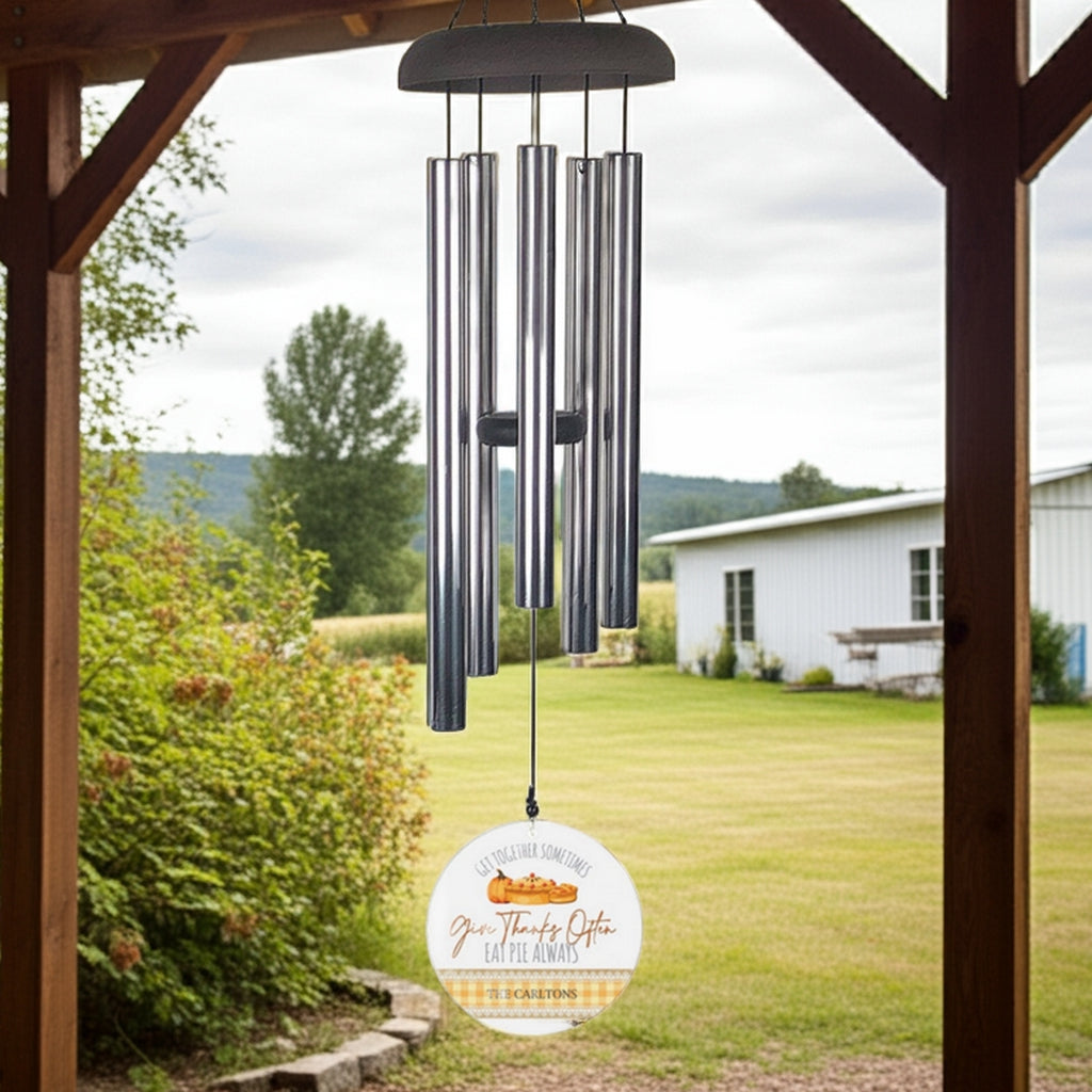 Wind chime with metal tubes hanging outdoors under wooden porch featuring personalized wind sail