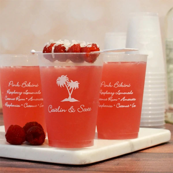 12 Oz Personalized Reusable Frosted Wedding Cups by Tippytoad with custom names and tropical design filled with pink lemonade