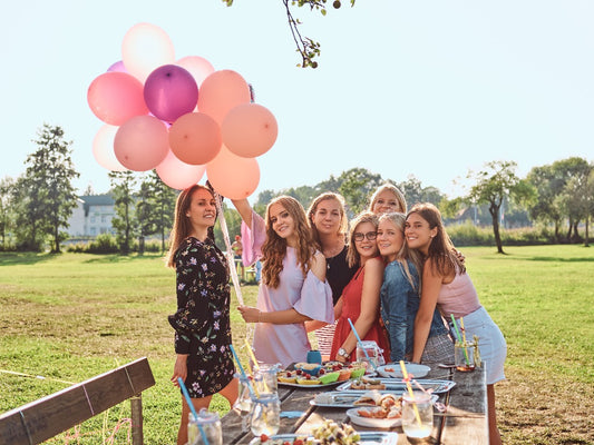 friends holding balloons over graduate at outdoor graduation party picnic