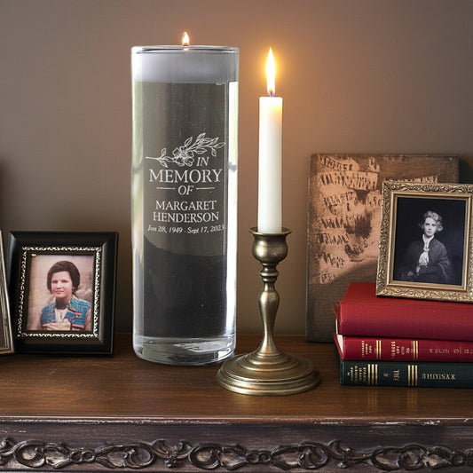 Memorial candles with personalized glass candle holder alongside framed photos and a lit taper candle on wooden surface