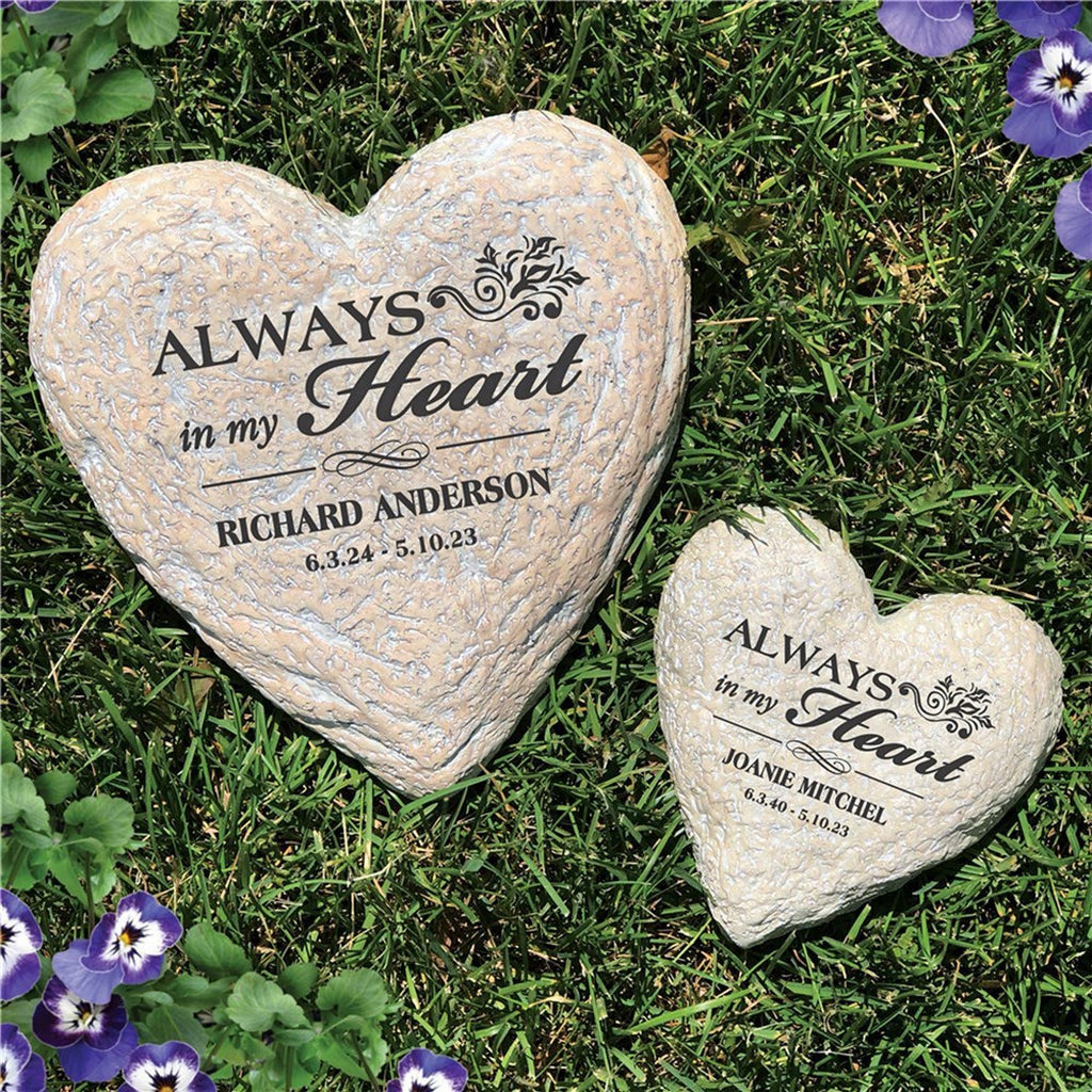 Personalized memorial garden stones in heart shapes with engraved names and dates on grass with purple flowers