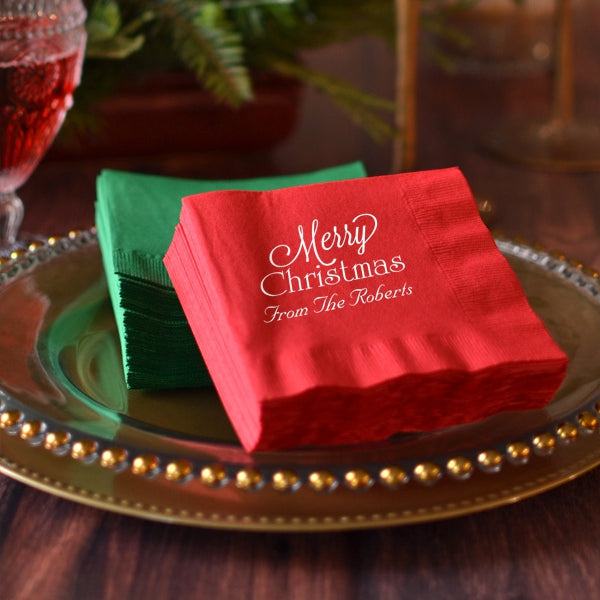 Personalized Christmas napkins in red and green with festive text on a decorative gold plate