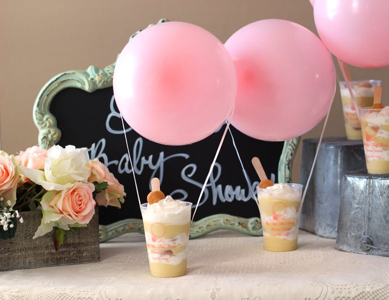 Personalized baby shower cups with dessert, pink balloons, flowers, and chalkboard sign for baby shower favors