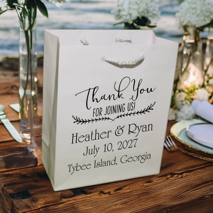 Personalized white wedding welcome bags with Thank You script and couple names on seaside wooden reception table