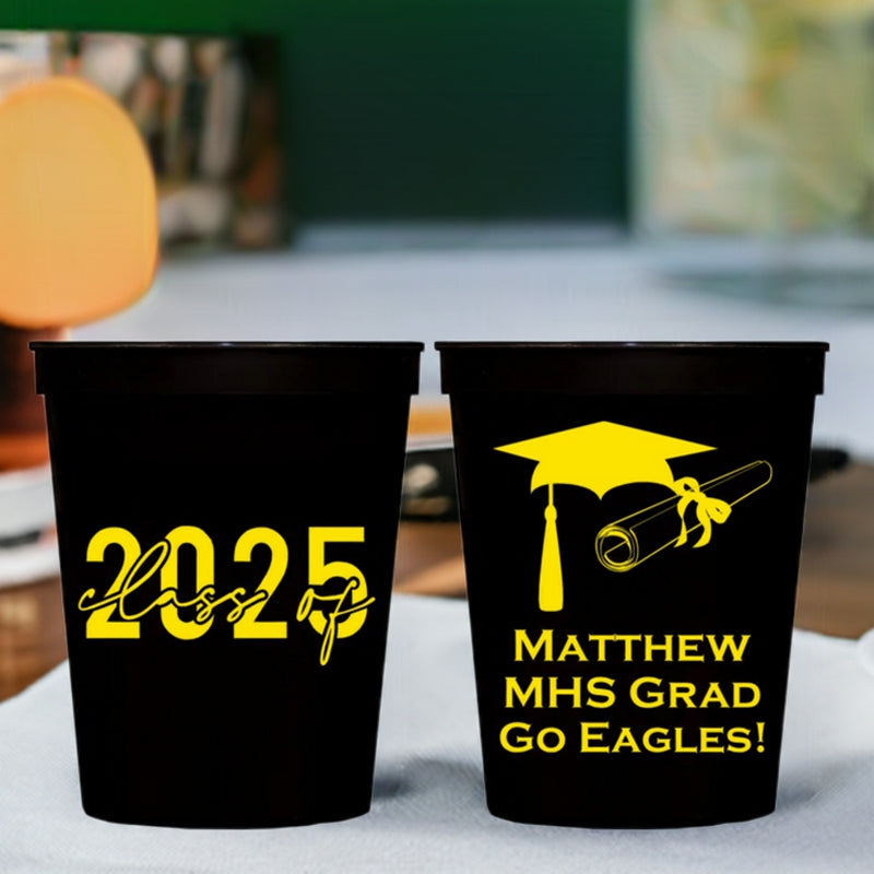 Black plastic graduation stadium cups personalized with Class of 2025 clip art on front side and Graduation Cap and Diploma clip art, graduate name and high school on back side in yellow print