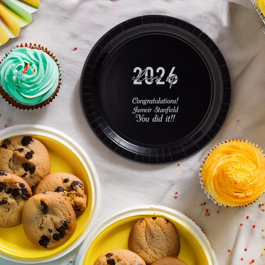 Black 7 Inch paper graduation snack plate personalized with "Class of 2026" design and text "Congratulations! [Graduate Name], You did it!" in silver print with cookies and cupcakes