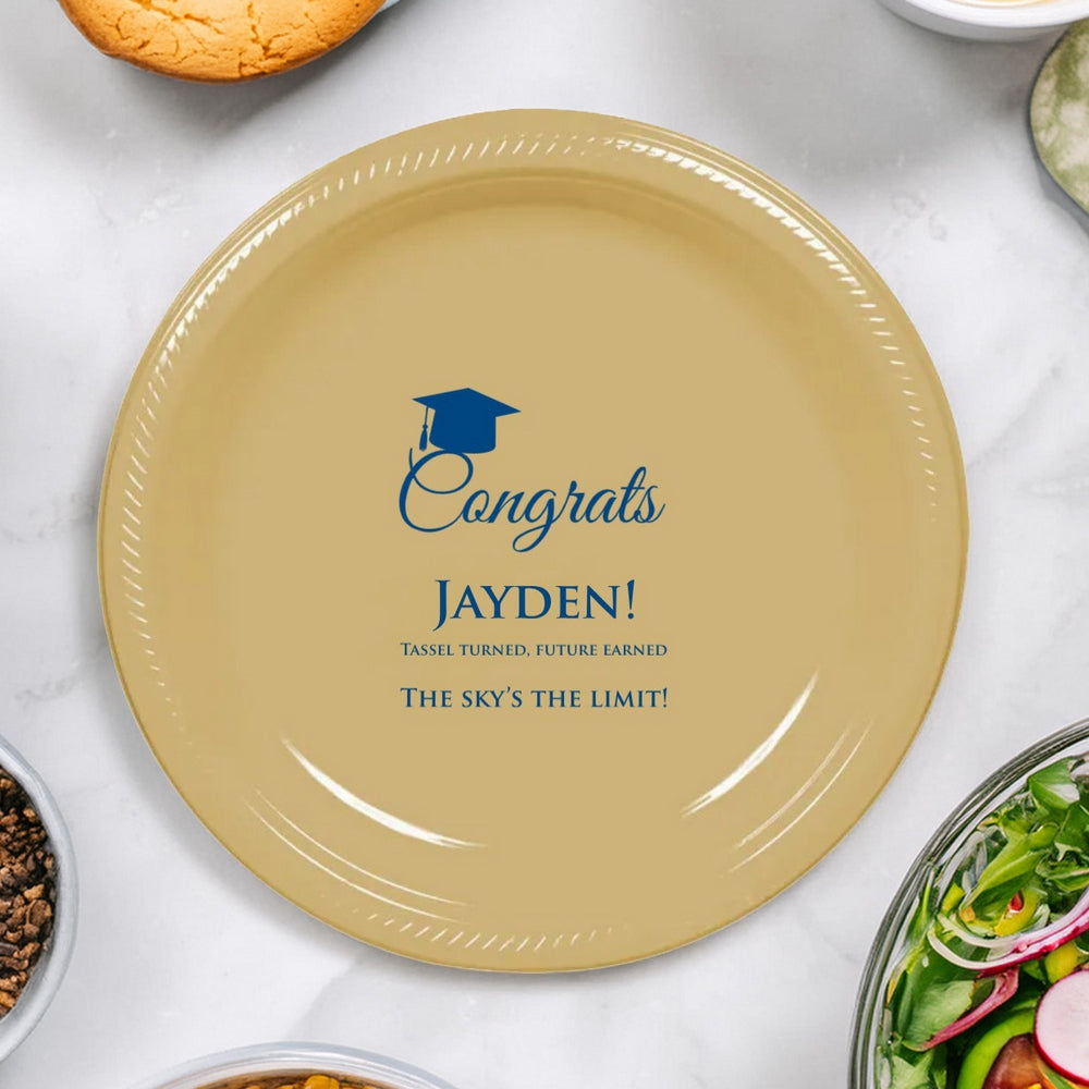 This elegant beige graduation plastic dinner plate, personalized in blue print, honors the graduate with a motivational message: "Congrats [Graduate Name]! Tassel turned, future earned. The sky's the limit!" A graduation cap adds a festive touch, while the plate sits amidst a spread of fresh salad and cornbread, symbolizing a nourishing start to the graduate's limitless future!