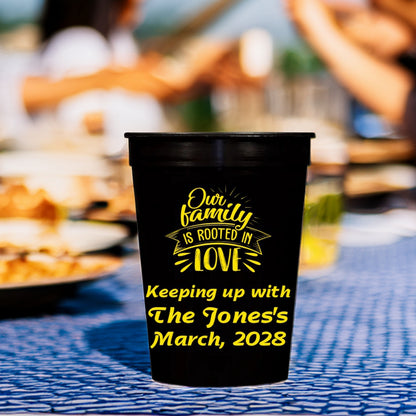 A black plastic cup personalized in yellow print with "Rooted In Love" family reunion graphic and text "Keeping up with The [Family Name]'s, March, 2028"