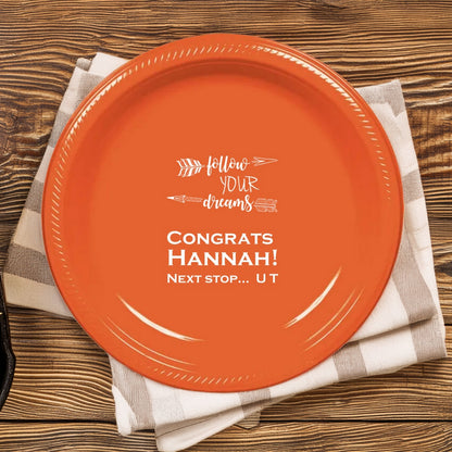 This bold orange graduation dinner plate personalized in white print inspires the graduate with the message: "Follow Your Dreams, Congrats [Graduate Name! Next Stop...UT." Adorned with arrow graphics, the graduation design encourages the graduate to aim high as she embarks on her journey to the University of Tennessee. Set on a rustic wooden picnic table with a checkered napkins, this customized dinner and picnic plate is a vibrant tribute to the graduate's bright future!