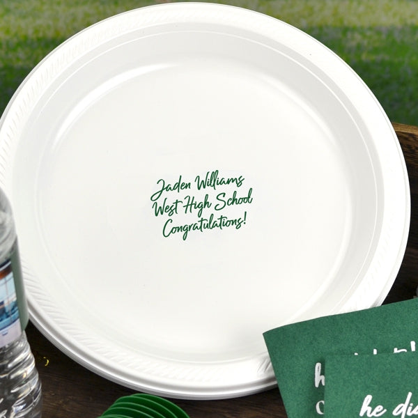 This classic white plastic graduation dinner plate personalized in green print proudly celebrates the graduate with the message: "[Graduate Name], West High School, Congratulations!" in elegant green text. Complimented with matching personalized napkins and set against a natural outdoor grad party backdrop, the customized plate marks a joyful milestone, inspiring the graduate to embrace the exciting journey ahead after graduating from high school!