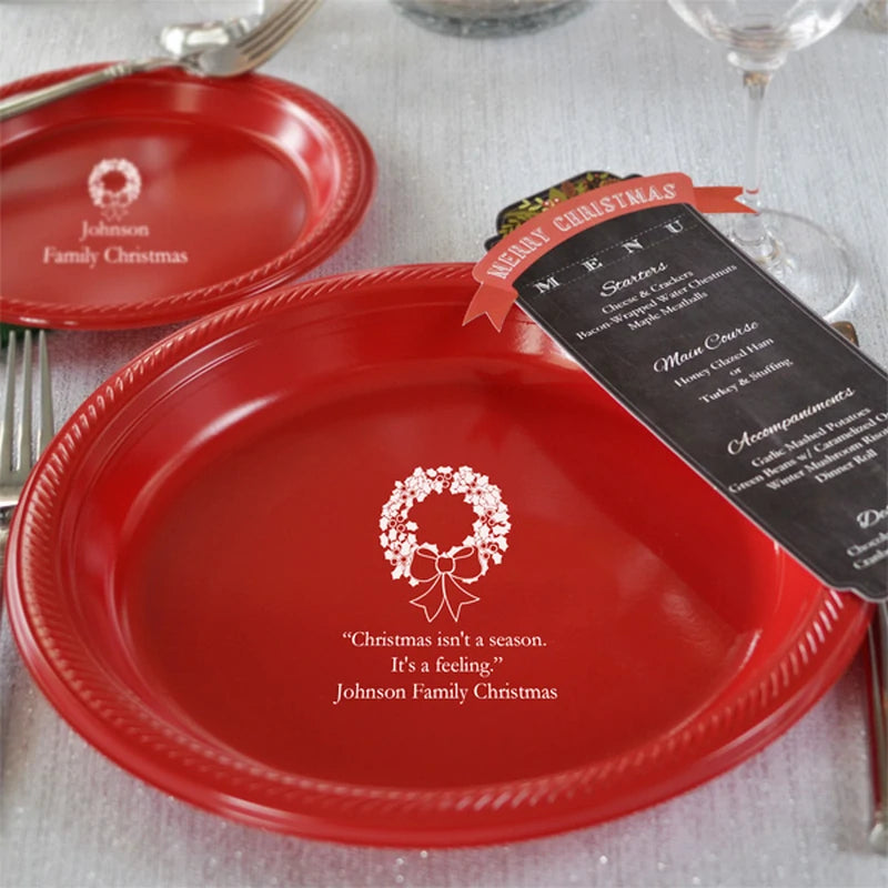 Red plastic Christmas dinner plate personalized with holiday wreath design and custom message in white print on beautifully decorated dinner table.