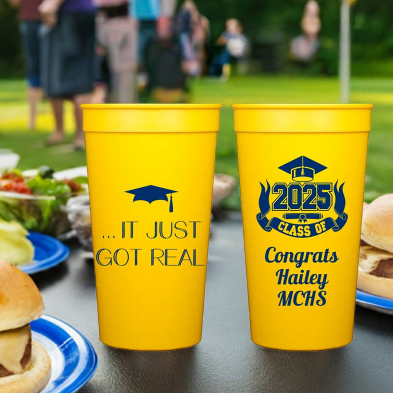 A set of yellow color plastic tumber cups customized for a graduation party with "...It Just Got Real" graphic design on the front side and a "Class of 2025 Graduation Cap and Diploma" with custom script text on the back side in Navy blue print