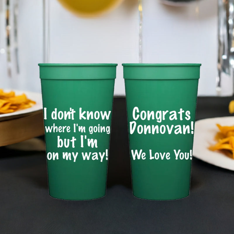 A set of green stadium cups personalized for a graduation party with four lines of custom text on the front side and three lines of custom text on the back side in white print.