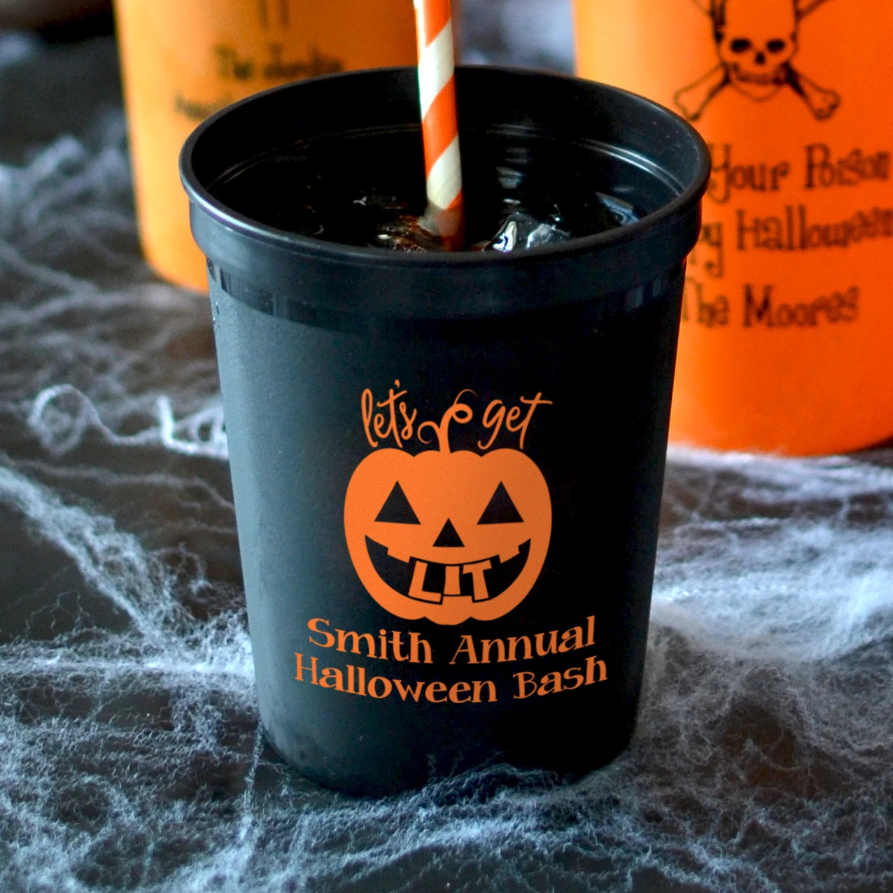 Black 16 oz. stadium cup personalized with 'Let's Get Lit Jack-O-Lantern' Halloween design and 2 lines of text in orange imprint color in the foreground and 22 oz personalized Halloween stadium cups in the background