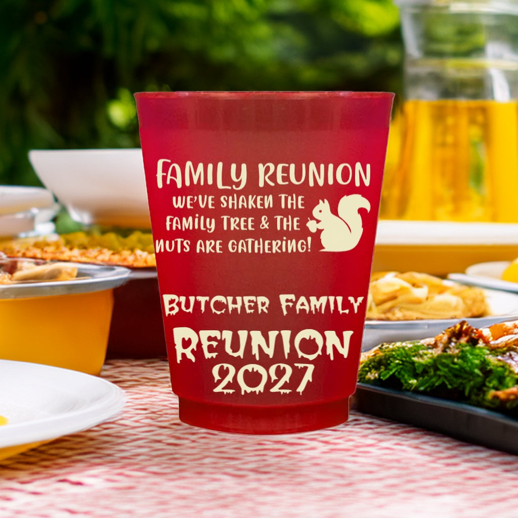 Red personalized family reunion cups with white text and squirrel graphic on picnic table with food