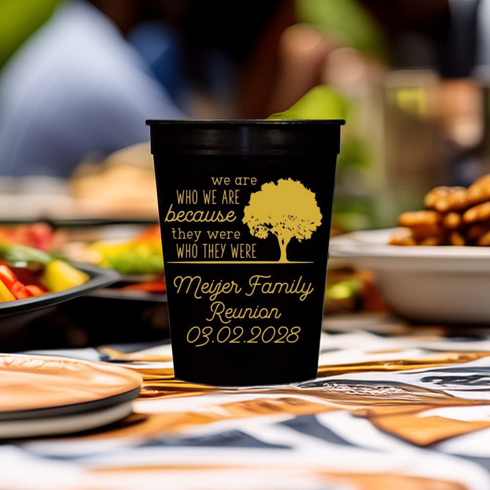 A black cup printed with "We Are Who We Are" Family tree graphic and text "[Family Name] Reunion, 03.02.2028" in gold print