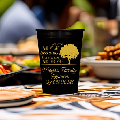 A black cup printed with "We Are Who We Are" Family tree graphic and text "[Family Name] Reunion, 03.02.2028" in gold print