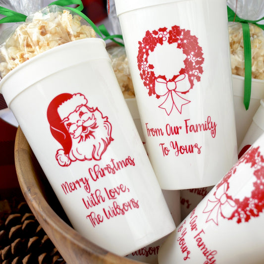 White 32 oz. stadium cups personalized with 'Classic Santa' Christmas design and three lines of text on the front and 'Wreath' holiday design and 2 lines of text on the back in red imprint color