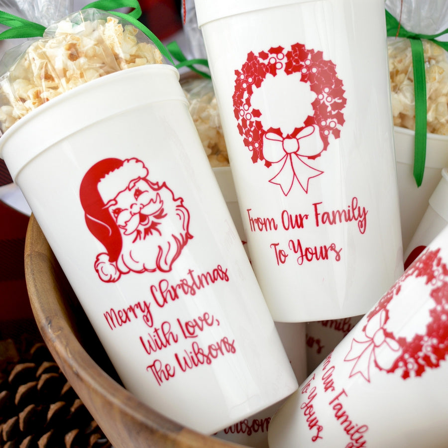 White 32 oz. stadium cups personalized with 'Classic Santa' design and three lines of text on the front and 'Wreath' design and 2 lines of text on the back in red imprint color