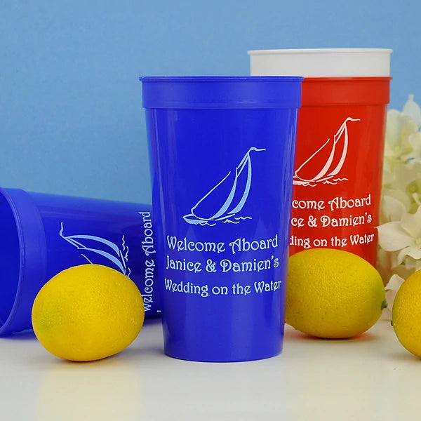Blue 32 oz. stadium cup personalized with 'Sailboat' design and 3 lines of text in pastel blue imprint and red cup in ivory imprint color for on the water theme wedding reception