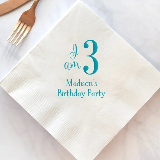 White paper beverage napkin personalized for toddler birthday with i am 3 design and 2 lines of text in teal print