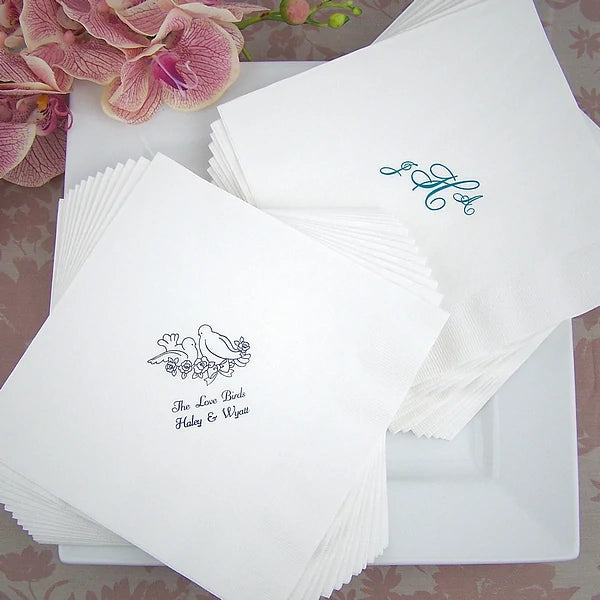 White linen feel wedding dinner napkins personalized with lovebirds design and 2 lines of text in black print on the left side of dinner plate and monogram design in hunter green print on right side of plate