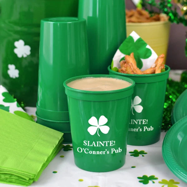 Green 16 oz. saint patricks day party cups personalized with shamrock design and 2 lines of text in white print on party table